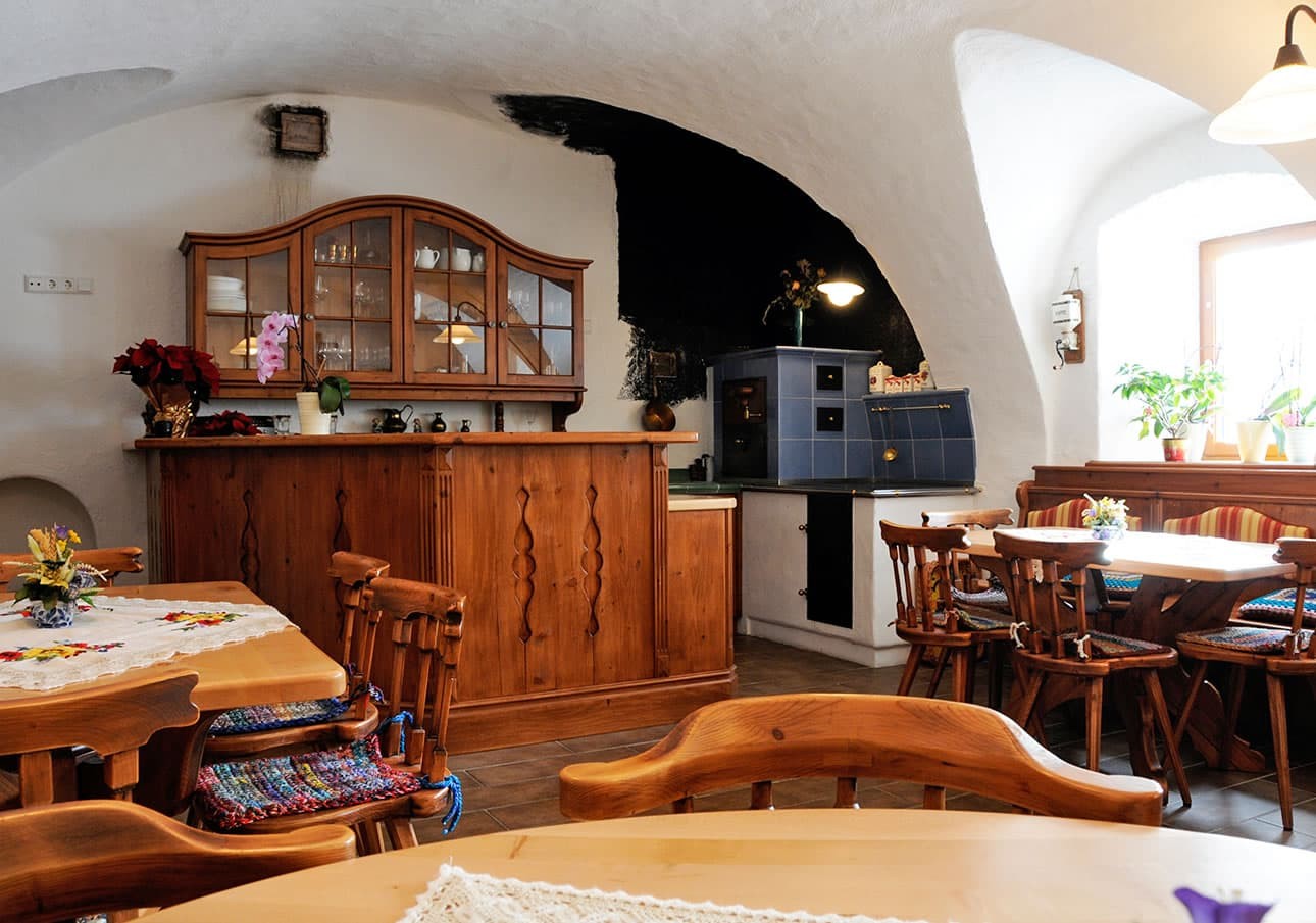 Gemütliche, rustikale Stube mit Holzmöbeln, Kachelofen und Pflanzen auf den Tischen