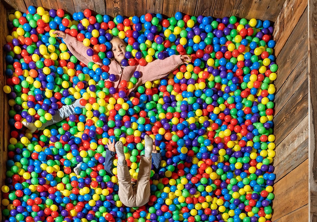 Zwei Kinder spielen in einem Becken voller bunter Bälle im Spielestadl am Bauernhof Prechtlhof