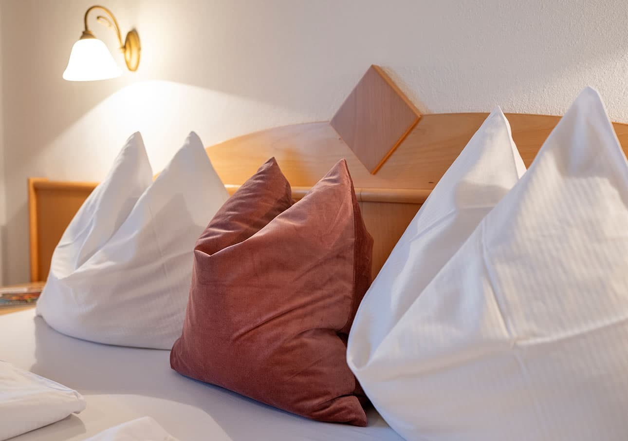 Three white pillows and a red pillow on a bed with a wooden headboard