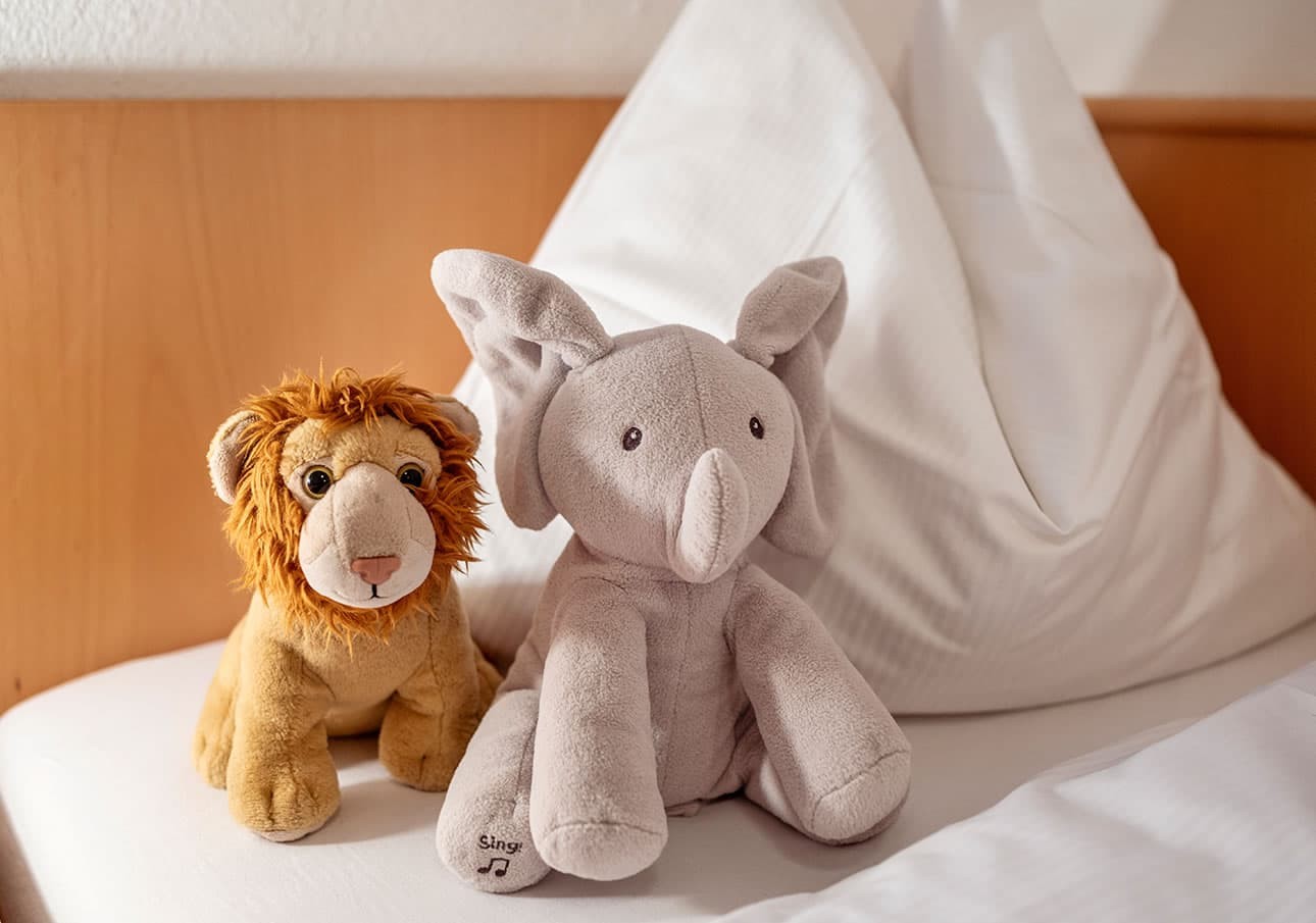 Plush lion and elephant toys sit together on a neatly made bed