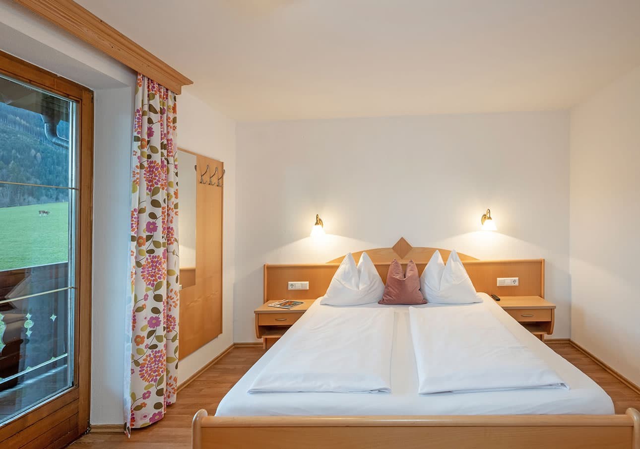 Cozy bedroom with a double bed, floral curtains, and wooden accents