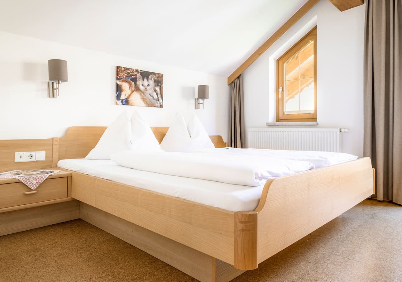 Bright bedroom with a wooden bed, white linens, and a window with curtain