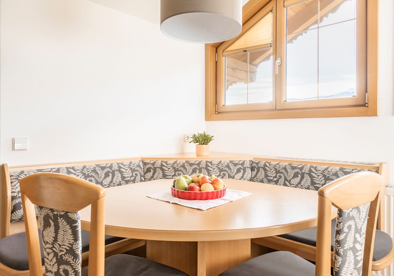 Wooden dining area with a bowl of fruit and window in the background