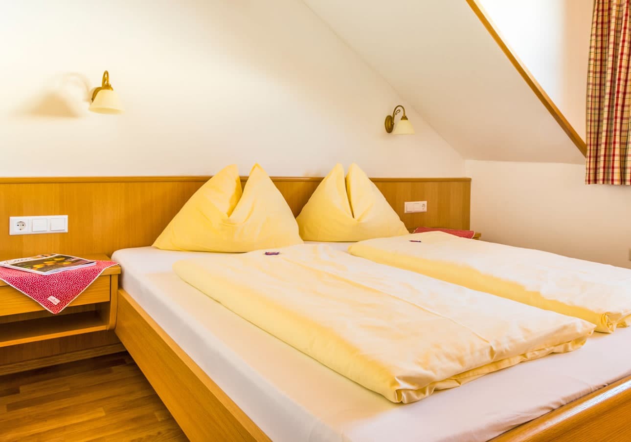Cozy bedroom with a sloped ceiling, two yellow pillows, and a neat wooden bed