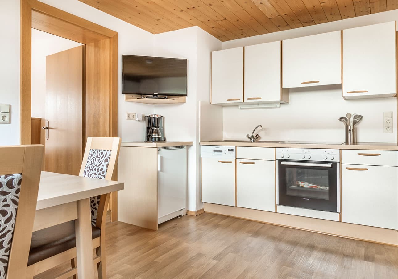 Small modern kitchen with white cabinets, a TV, and a dining table with patterned chairs