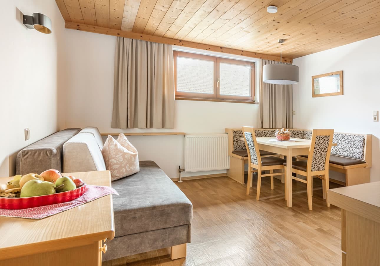 Cozy dining and living area with wooden ceiling, table, chairs, and a gray couch