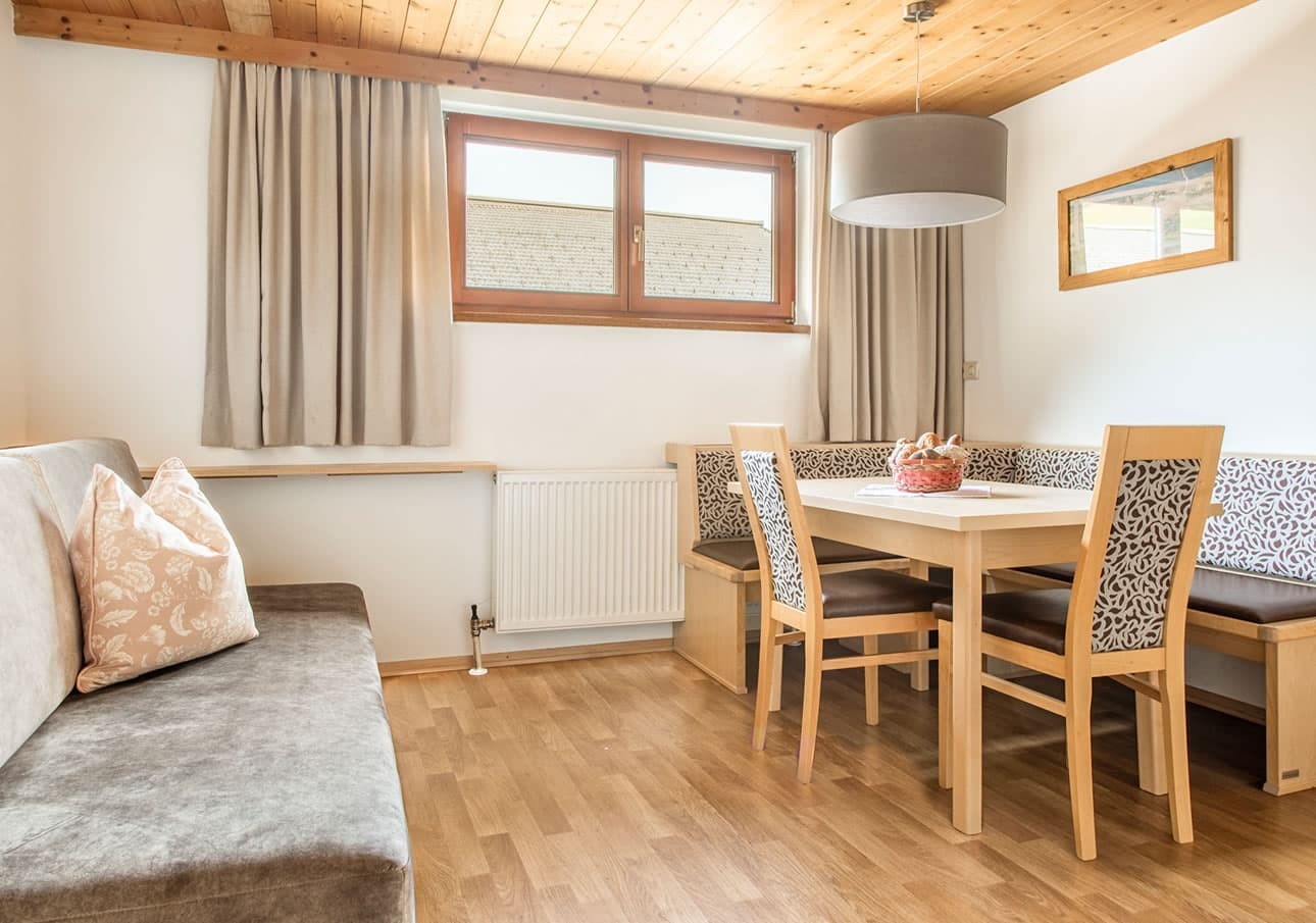 Bright dining area with wooden table, chairs, and sofa under a window with beige curtains