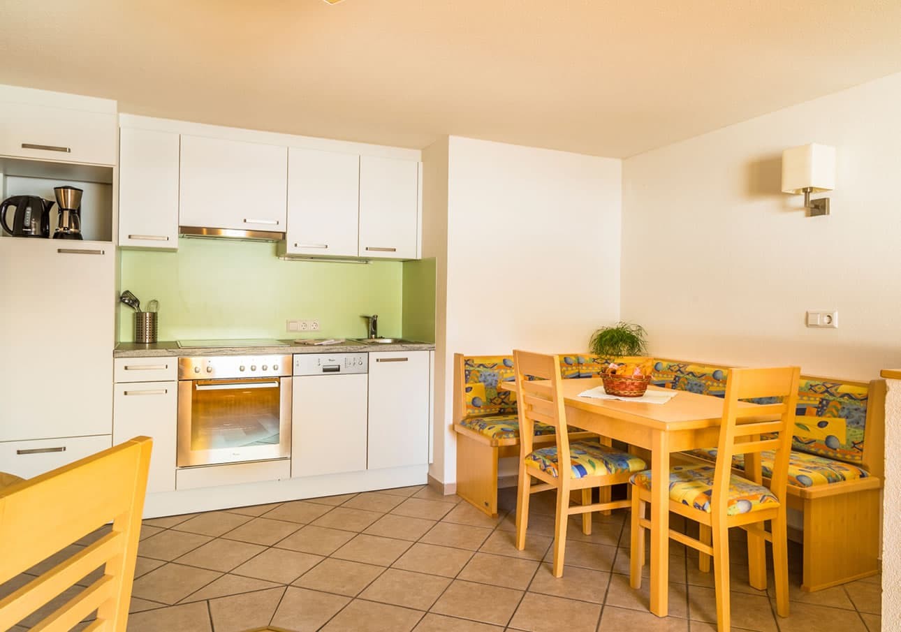 Modern kitchen with white cabinets and cozy dining nook with colorful cushions