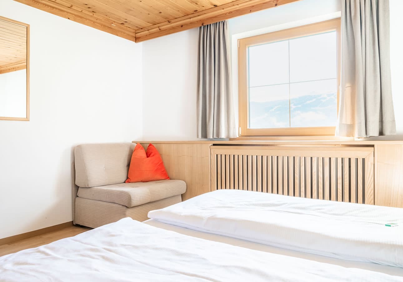 Bright bedroom with a wooden ceiling, bed, armchair, and a window with curtains