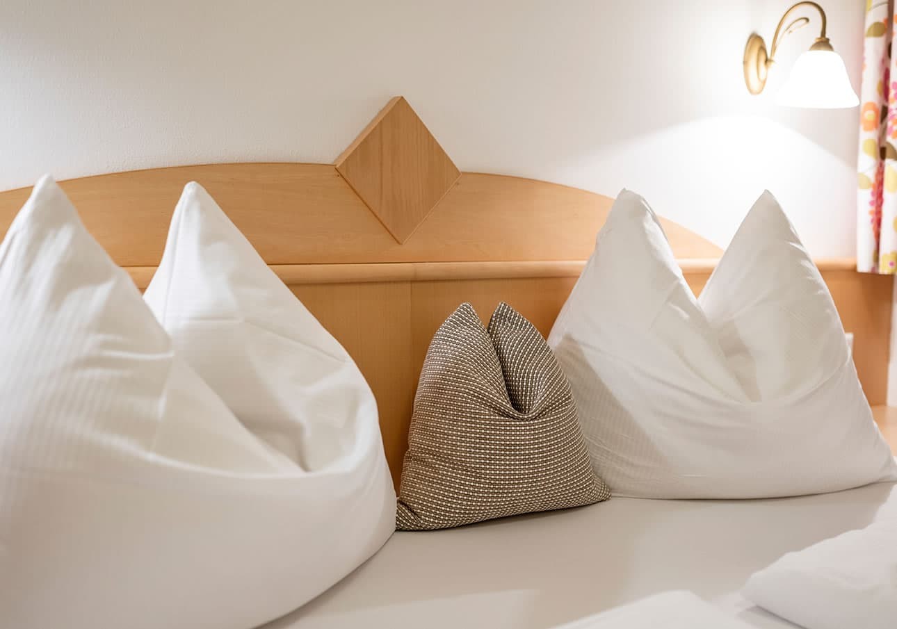 Three pillows on a bed, two white and one grey, under a wooden headboard