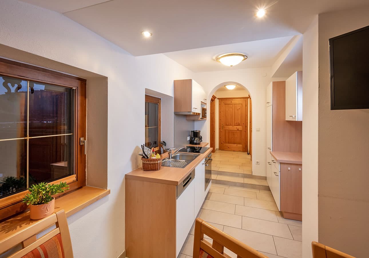A narrow kitchen with wooden cabinets and a window, leading to a wooden door