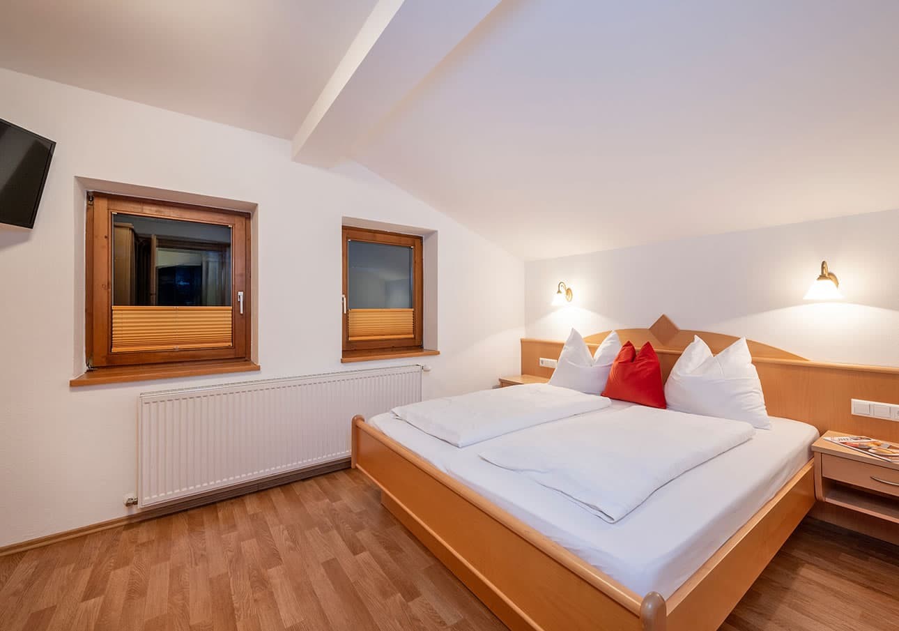 Cozy bedroom with a neatly made double bed, bedside lamps, and two windows