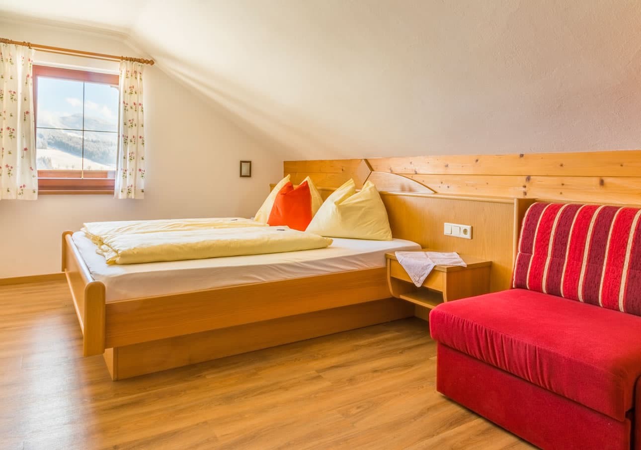A cozy bedroom with wooden furniture, bright pillows, and a red cushioned chair
