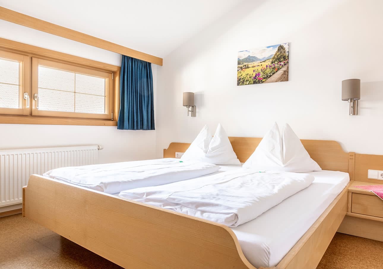 Bright bedroom with a double bed, wooden furniture, and a small landscape picture on the wall