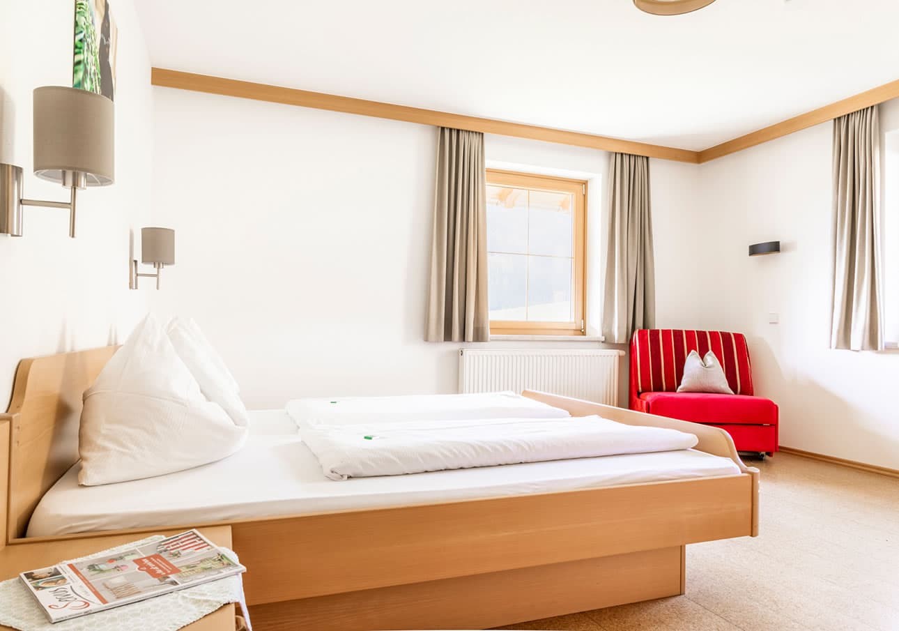 A bright bedroom with a double bed, red armchair, and large windows