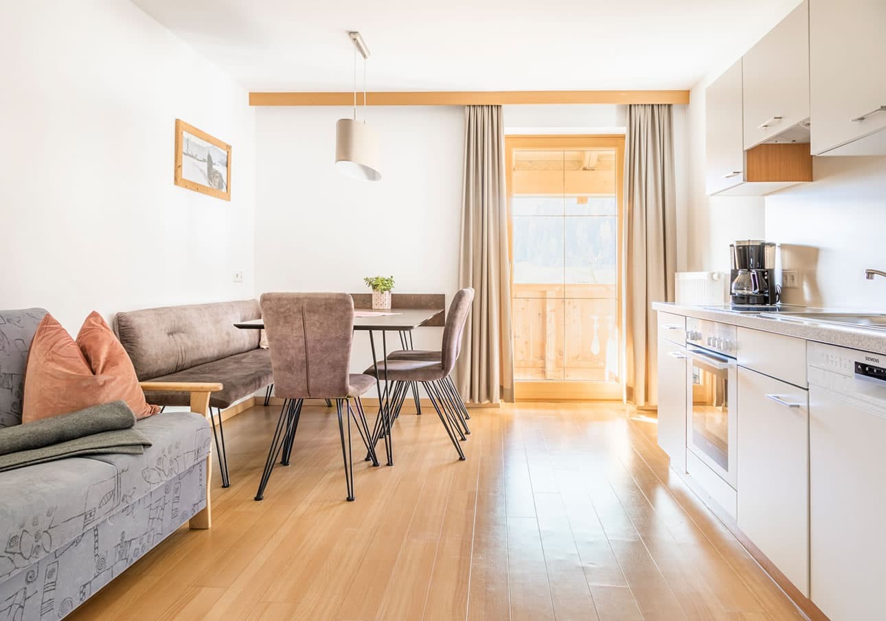Modern kitchen and dining area with light wood flooring and a door leading to a balcony