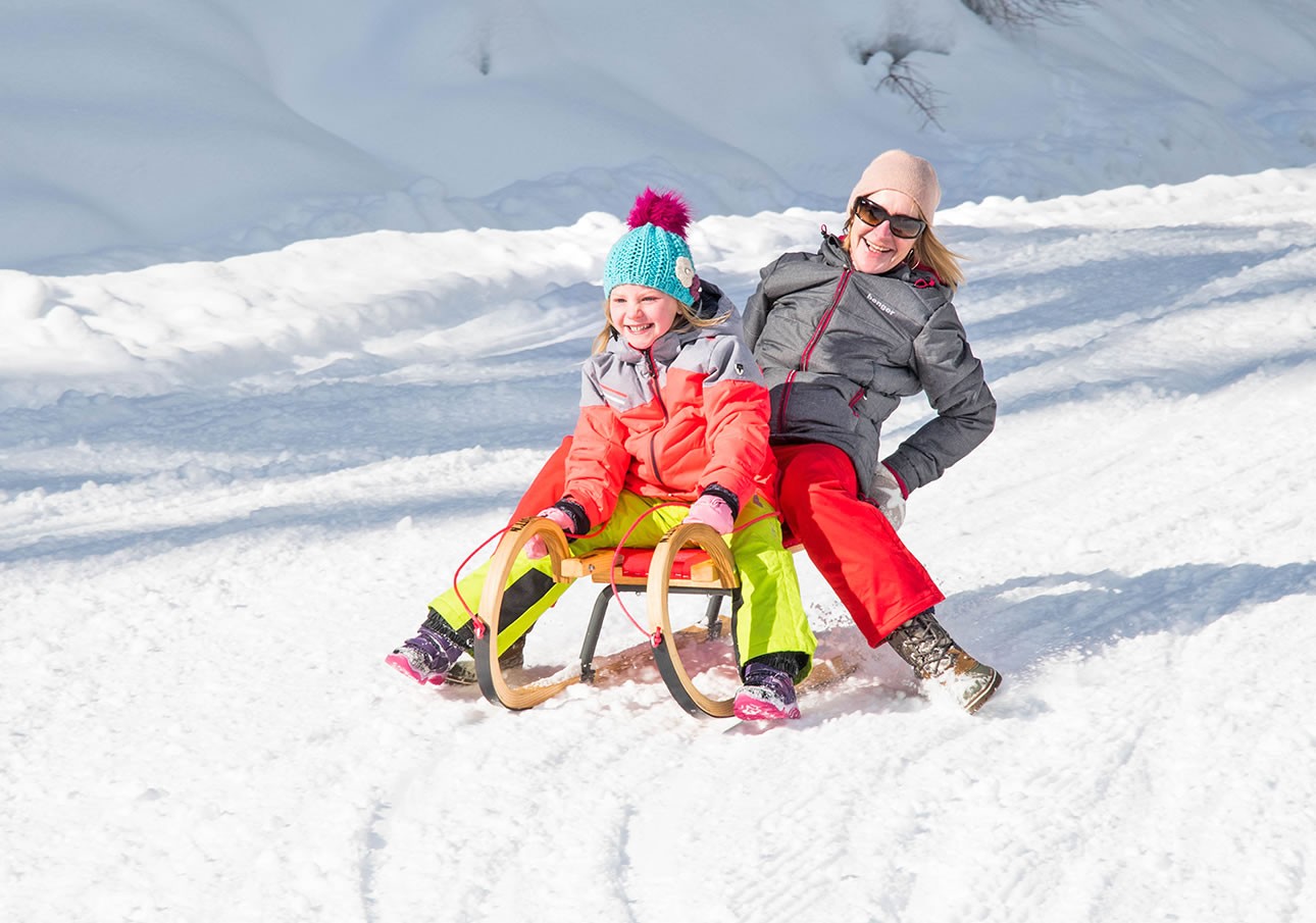 A smiling woman and child sledding down a snowy hill
