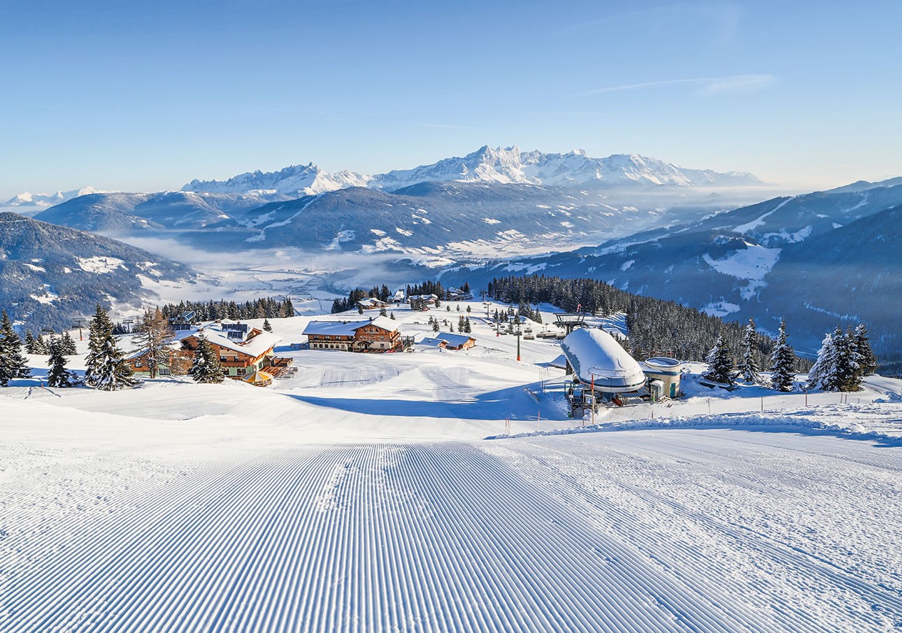 Snow-covered ski resort with mountains and chalets under a clear blue sky