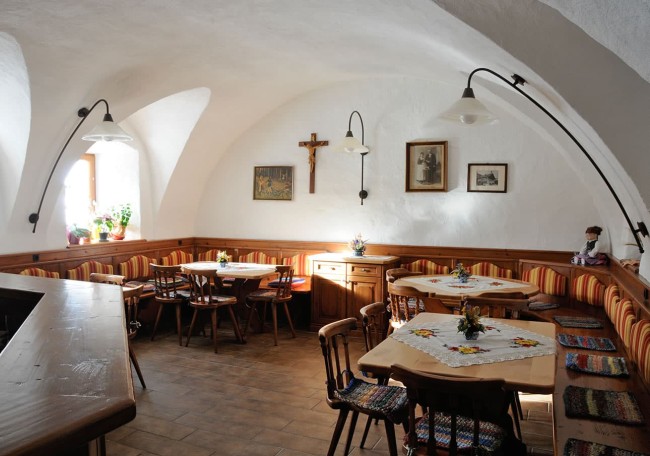 Gemütliche Gaststube mit Holzmöbeln und religiösen Wanddekorationen in sanftem Tageslicht