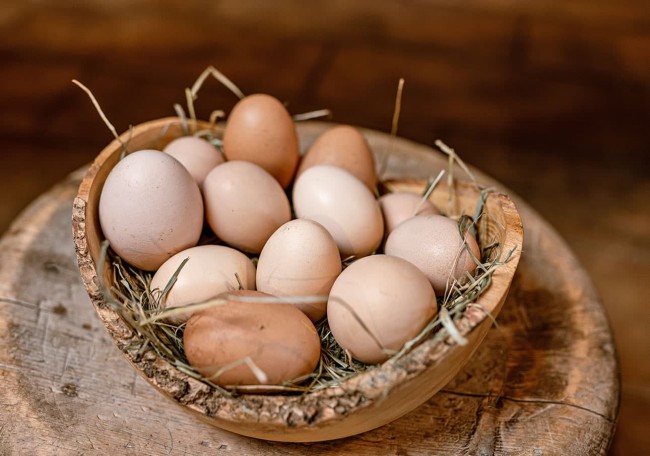 Eine Schale mit Eiern und Heu steht auf einem rustikalen Holztisch