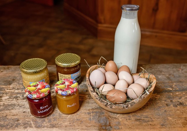 Eine Flasche Milch, ein Korb voller Eier und vier Gläser Marmelade auf einem Holztisch
