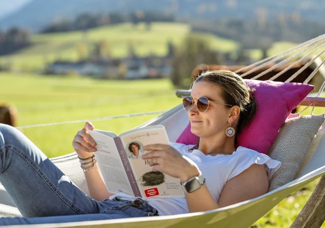 Eine Frau entspannt in einer Hängematte und liest ein Buch