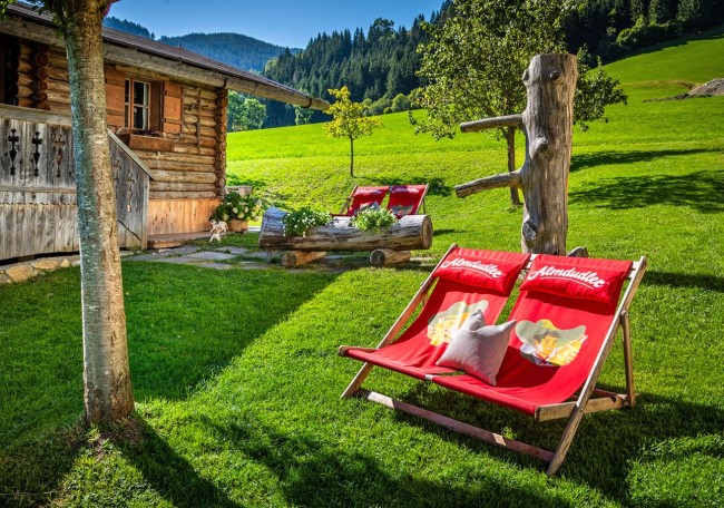Holzhütte mit Liegestühlen auf einer grünen Wiese in den Bergen