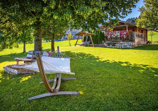 Grüne Wiese mit Hängematte, rustikalem Haus und Blumen im Sonnenschein