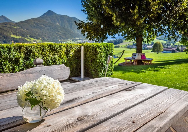 Holztisch mit Blumen vor Landschaft mit Bergen und grünem Gras im Hintergrund