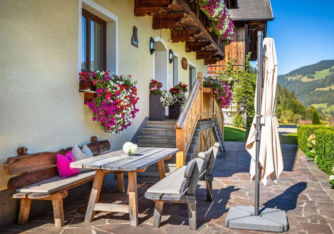 Gemütliche Terrasse mit Holzbänken, Tisch und bunten Blumenkästen an einem sonnigen Tag