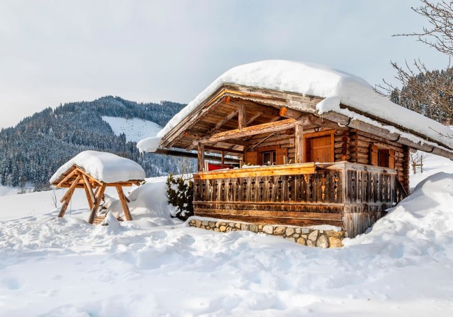 Holzhütte und überdachter Holzstapel im verschneiten Berggebiet