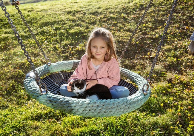 Mädchen sitzt auf einer Schaukel und streichelt eine schwarz-weiße Katze