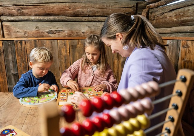 Eine Frau und zwei Kinder spielen an einem Tisch im Spielestadl