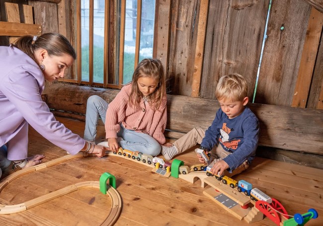 Drei Kinder spielen mit einer Holzeisenbahn auf einem Holzboden im Spielestadl