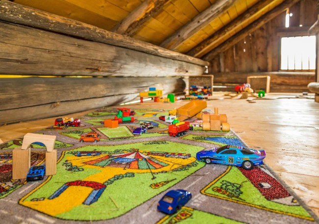 Ein Dachboden mit Spielzeugautos und Bauklötzen auf einem bunten Teppich im Spielestadl