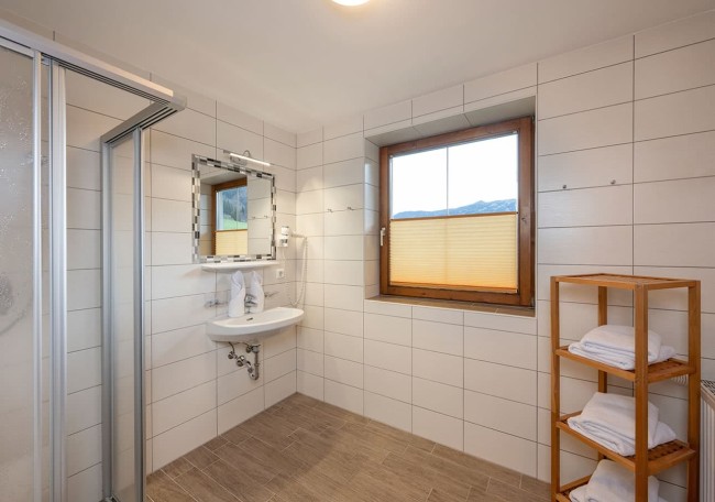 Helles Badezimmer mit Dusche, Waschbecken und Regal voller Handtücher