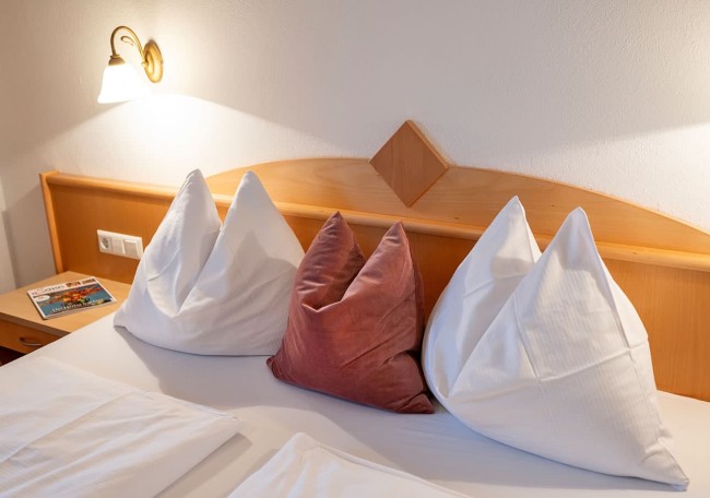 Ein gemütliches Bett mit vier Kissen und einer Lampe auf einem hölzernen Nachttisch