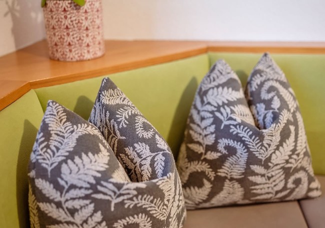 Zwei graue Kissen mit weißen Blattmustern auf einem grünen Ecksofa