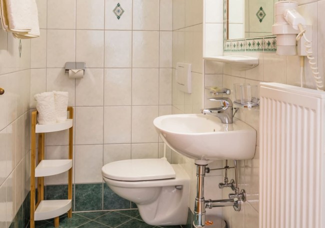 Kleines, sauber gefliestes Badezimmer mit Toilette, Waschbecken und Regal