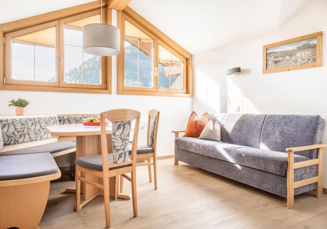 Helles Wohnzimmer mit Holzdeko, Eckbank, Sofa und Panoramafenstern mit Bergblick