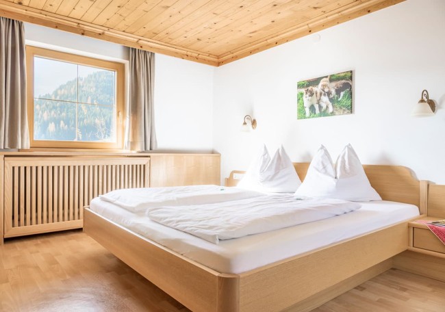 Helles Schlafzimmer mit Holzmöbeln und großem Fenster, das Blick auf die Berge bietet