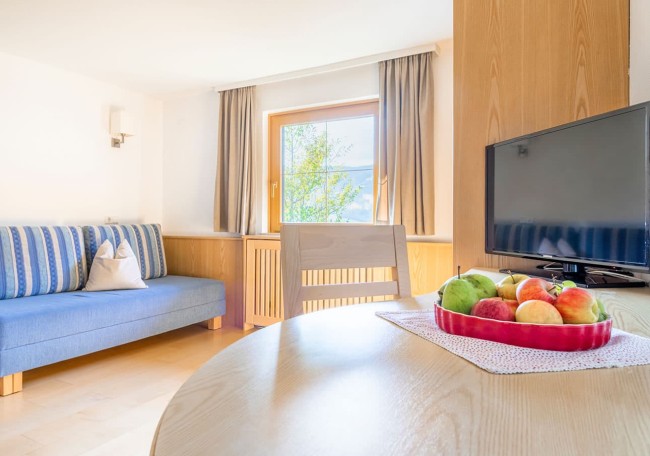 Helles Wohnzimmer mit Sofa, Fernseher und Früchteschale auf einem Holztisch