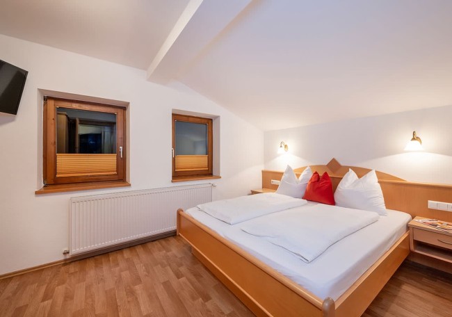 Helles Schlafzimmer mit Holzbett, zwei Fenstern und Nachttischen, schlicht und gemütlich