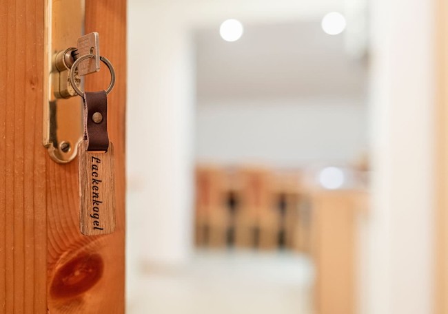 Schlüssel steckt mit Schlüsselanhänger "Lackenkogel" in einer Holztür vor einem unscharfen Raum