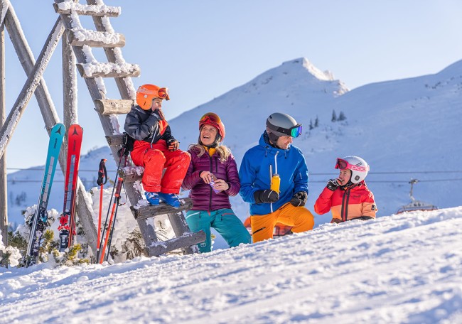 Eine Familie in bunter Skiausrüstung lacht im Schnee vor einer Winterlandschaft