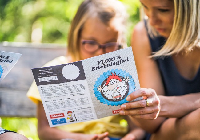 Eine Frau und ein Kind lesen gemeinsam eine Broschüre über Flori's Erlebnispfad