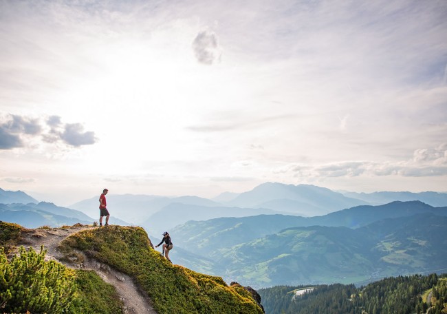 Zwei Wanderer stehen auf einem Bergpfad mit weitem Blick über bewaldete Hügel