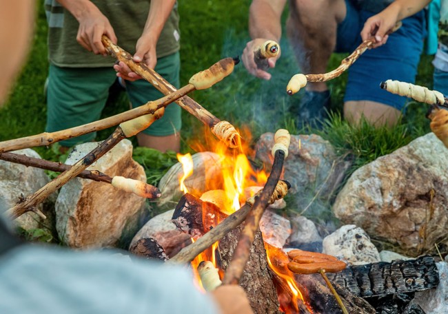 Menschen rösten Brot an Stöcken über einem Feuer im Freien