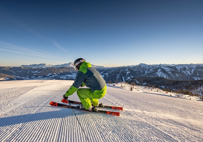 Ein Skifahrer in grüner Kleidung fährt auf einer sonnigen Piste in den Bergen