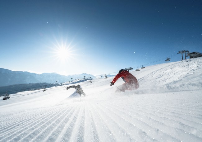 Zwei Skifahrer fahren bei sonnigem Wetter auf einer Skipiste